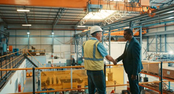 Business people at an industrial workshop shaking hands at a factory. Successful business man congratulating contractor for excellent work on maintenance, development and management.